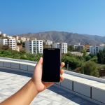A young person in Northern Cyprus using a smartphone to manage a successful online business, with modern buildings and clear skies in the background.